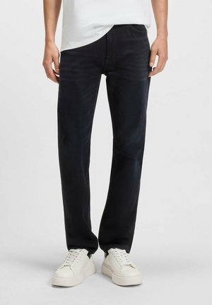 Dark denim jeans with a straight-leg fit, featuring subtle whiskering, traditional pockets, and a smooth, textured finish. Paired with white sneakers.