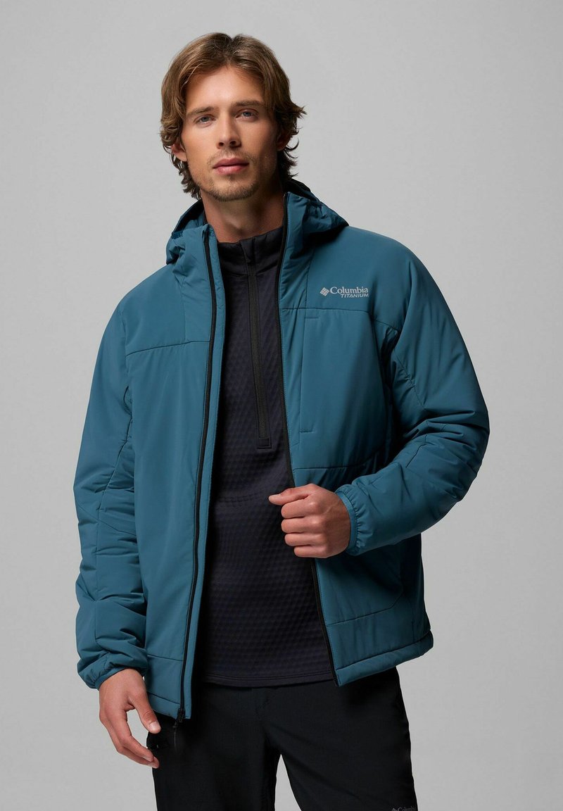 Türkise isolierte Jacke mit Kapuze, Reißverschluss und elastischen Bündchen. Getragen über einem schwarzen, strukturierten Oberteil, das Funktionalität und Komfort vereint.