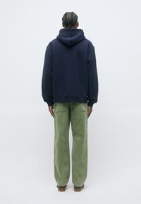 Felpa con cappuccio blu navy a vestibilità rilassata abbinata a pantaloni in corda a gamba larga verde chiaro. La texture è morbida e il design è semplice.