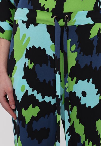 Bunte Hose mit einem abstrakten Muster in Blau, Grün und Schwarz. Sie verfügt über einen kontrastierenden Taillenbund mit Bändern und goldfarbenen Beschlägen.