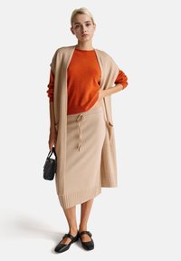 Beżowy sweter z dzianiny, pomarańczowy sweter oraz beżowa dzianinowa spódnica z prążkowanym dołem. Czarne buty na kostkę z paskiem i mała czarna torba.