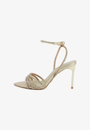 Sandalo beige con tacco alto, con sottili cinturini intrecciati che si incrociano sulle dita dei piedi e cinturino alla caviglia con una piccola fibbia.