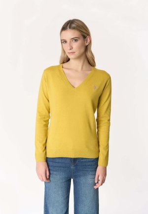 Maglione giallo a maglia con scollatura a V, maniche lunghe e dettaglio del logo sul petto. Abbinato a jeans di denim blu.