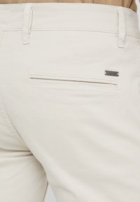 Bílé bavln�ěné kalhoty s jako kapsou na zadní straně se horizontálním otvorem a kovovým logem "BOSS". Hladká textura a přizpůsobený střih.