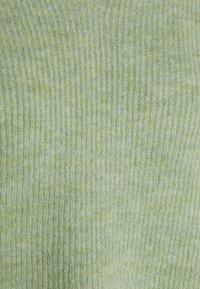 Tissu tricoté vert clair avec une texture côtelée, présentant de fines lignes horizontales. Le matériau semble doux et légèrement duveteux.
