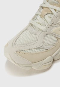 Baskets de sport beige clair en matière mesh et suède, avec des accents texturés, des lacets et une semelle arrondie.