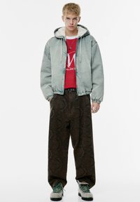Jachetă din denim de un albastru estompat, cu un căptușeală pufoasă albă, asortată cu pantaloni largi cu model maro și pantofi gri cu șireți verzi.