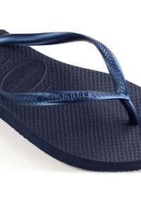 Marineblaue Flip-Flops mit strukturiertem Fußbett und breiten Gummiriemen, die ein Chevron-Muster aufweisen, sowie einem prägenden Markenlogo auf dem oberen Riemen.