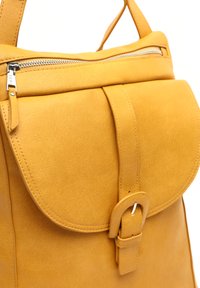 Žltý kožený batoh s poklopom, magnetickou sponou a strieborným zipsom. Hladká textúra s čistým prešívaním.