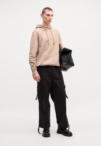 Beige hoodie met een voorzak, gecombineerd met zwarte cargo shorts met zijzakken en trekkoorden, aangevuld met zwarte schoenen.