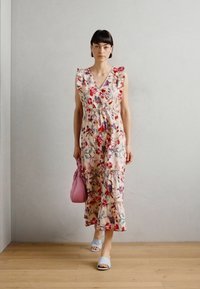 Rochie maxi florală cu mâneci volan, bază crem, flori roșii și mov, design stratificat. Asortată cu sandale bleu deschis și o geantă roz.