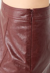 Bordeaux kunstleren rok met een gladde textuur, voorzien van een zijrits en subtiele stiksels langs de tailleband en naden.