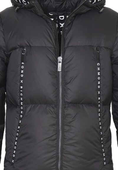 Giubbotto imbottito nero con chiusura a zip sul davanti, due tasche laterali e dettagli del logo sul petto e sulla manica. Texture liscia con design imbottito.