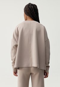 Felpa over-size beige chiaro con spalle scese, caratterizzata da una cucitura dritta sul retro e un tessuto morbido e texturizzato.