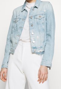 Veste en denim bleu clair avec des détails délavés, col classique et fermeture à boutons. Dotée de deux poches poitrine et d'un ourlet effiloché.