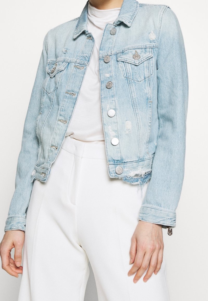 Veste en denim bleu clair avec des détails délavés, col classique et fermeture à boutons. Dotée de deux poches poitrine et d'un ourlet effiloché.