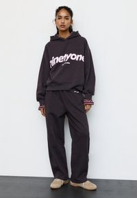 Tummanharmaa huppari, jossa on vaaleanpunainen "ninetyone"-logo, yhdistettynä samaa sarjaa oleviin väljälahkeisiin housuihin. Hupparissa raidalliset hihansuut ja pehmeä, teksturoitu kangas.