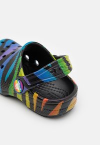 Barefootové ponožky v pestrých pruhách s černým základem, vyrobené z gumového materiálu, s nastavovacím popruhem na patě a kulatým logem na boku.