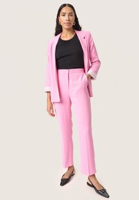Suit rosa su misura con una giacca aderente e pantaloni dritti. Top nero a coste sotto, abbinato a scarpe slip-on nere in vernice.