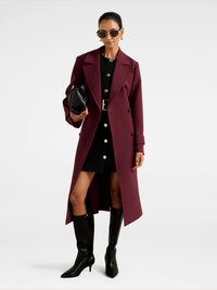 Burgundia topelt nööridega jope kuldsete nupukestega, kombineeritud musta Kleit ja mustad põlvikud, kandes musta käekotti.