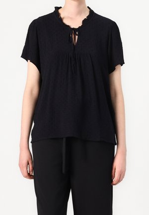 Blusa nera a maniche corte in tessuto textured, con scollatura a occhio di bue e bordi a ruffle. Vestibilità ampia con dettagli arricciati nella parte frontale.