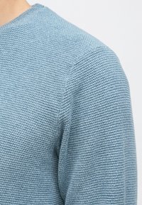 Svetlomodrý pletený sveter s textúrovaným rebrovaným vzorom, okrúhlym výstrihom a priliehavým strihom, zdôrazňujúci mäkkú a priedušnú tkaninu.