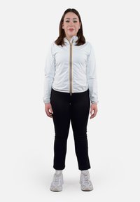 Giacca atletica bianca con zip, dotata di una zip oro e nera, abbinata a leggings neri e scarpe da ginnastica bianche, vista frontale.