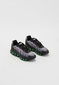 Ciemnoszare trampki z teksturowaną cholewką, zielonymi akcentami i charakterystycznymi okrągłymi poduszkami amortyzującymi. Posiadają czarne sznurowadła oraz kultowe logo.