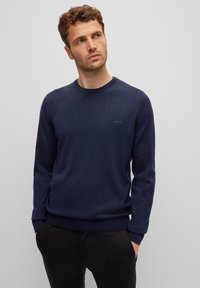Navy blue sweater with a round neck, long sleeves, ribbed cuffs, and hem, featuring a subtle logo on the chest. Soft knit texture.