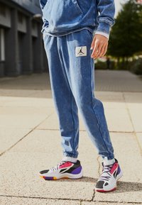 Hellblaue Jogginghosen mit einem Jordan-Logo-Patch; weicher Stoff, elastischer Bund und Bündchen. Kombiniert mit mehrfarbigen Sportschuhen.