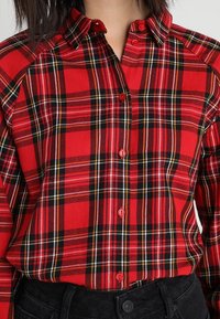 Chemise à carreaux rouges avec touches de noir et de jaune, dotée d'un col et de boutons contrastants. Fabriquée en tissu doux et tissé.