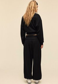 Sort kort sweatshirt og bukser med vidde, der har en blød tekstur og en afslappet pasform, kombineret med hvide træningssko.