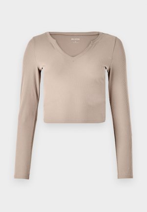 Dolga majica s kratkim krojem iz svetlo bež rebraste tkanine z V-izrezom in minimalističnimi šivi na ovratniku.