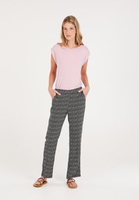 T-shirt rosa chiaro con maniche a cappuccio, abbinato a pantaloni a fantasia bianco e nero con tasche laterali e taglio dritto. Sandali marroni.