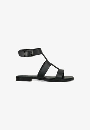 Sandal in pelle nera con cinghia alla caviglia, caratterizzata da tre ampiezze di fascia nella parte anteriore, suola piatta e dettagli in fibbia metallica.