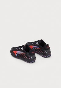 Black athletic shoes with red and purple accents, mesh upper, textured sole, and a distinctive wave design along the sides.