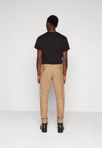 Camiseta negra de manga corta combinada con pantalones de tejido en color beige, con un bolsillo trasero y detalles sutiles, completada con zapatos negros.