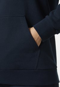 Námořnický modrý svetr s jemnou texturou, se přední kapsou, žebrovanými manžetami a rovný lem. Jednoduchý, nezdobený design.