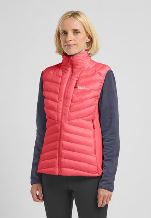 Gilet imbottito senza maniche di un vivace colore rosa con colletto alto, frontale con zip e tasche laterali. Indossato sopra una maglietta a maniche lunghe blu navy.