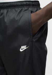 Μαύροι αθλητικοί παντελόνια Nike με ελαστική μέση, τσέπες με φερμουάρ στο πλάι και λευκό λογότυπο στο κάτω αριστερό πόδι. Ομαλό, ελαφρύ υλικό.