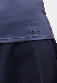 Κοντινή λήψη σκούρου μπλε αθλητικού ενδύματος με την επιγραφή "BORG" ανάγλυφη κοντά στο τελείωμα, που δείχνει την υφή του υφάσματος και τις λεπτομέρειες της ραφής.