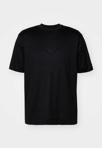 Black t-shirt with short sleeves, round neckline, and a textured logo at the chest. Made from a smooth, lightweight fabric.