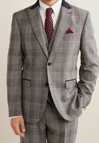 Completo grigio a quadri con finitura testurizzata. Presenta un colletto nero, una cravatta bordeaux con pois e un fazzoletto coordinato.