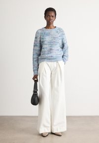 Blau-lila gestrickter Pullover mit strukturiertem Muster; weiße weite Hose; schwarze Tasche; beigefarbene spitze Ballerinas; minimalistischer Hintergrund.