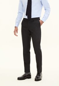 Dunkelgraue maßgeschneiderte Hosen aus glattem Stoff, mit einem Slim-Fit-Design und flachem Bund, getragen mit einem hellblauen Hemd und schwarzen Schuhen.