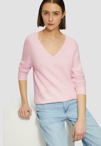 Roze gebreide trui met een V-hals, driekwartmouwen en een losse pasvorm, gecombineerd met lichtblauwe denim jeans. Gelaagd ribbenontwerp.