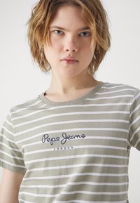 Olivengrønn og hvit stripete bomull t-skjorte med rund hals. Har "Pepe Jeans London" logo i marineblått på forsiden.