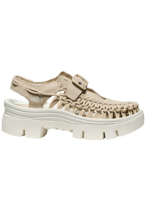 Beige gewebte Sandale mit dicker weißer Sohle, verstellbarem Schnallenriemen und offenem Absatz, entwickelt für legere Outdoor-Benutzung.