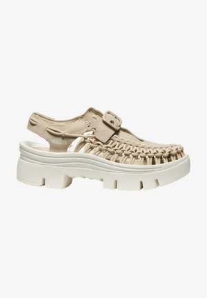 Beige gewebte Sandale mit dicker weißer Sohle, verstellbarem Schnallenriemen und offenem Absatz, entwickelt für legere Outdoor-Benutzung.