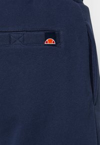 Marineblauer Sweatshirtstoff mit weicher Textur, mit einem kleinen Logo-Patch in rot und weiß auf der Rückseite.